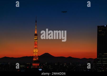 Ein Flugzeug steigt in einen orangefarbenen Sonnenuntergang ab, während es sich dem tokioter Turm nähert, mit der Silhouette des fuji-Berges im Hintergrund Stockfoto