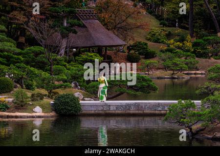 Shukkei-en japanischer Garten in hiroshima eine junge Dame in einem grünen Kimono, die auf einem Steinsteg steht, spiegelt sich im Wasser des Teiches Stockfoto