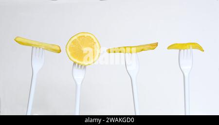 Diätkonzept, Reihe fettiger Pommes frites auf Plastikgabeln und eine Scheibe Zitrone. Junkfood versus gesunde Ernährung, Gewichtsreduktion für den Frühling conc Stockfoto