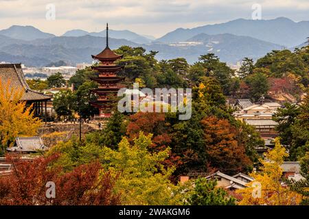 Blick vom Hügel der Insel miyajima auf den itsukushima-Schrein und die fünfstöckige Pagode umgeben von farbenfrohen Herbstlaub und Bergen von hiroshima BA Stockfoto