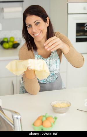 Glückliche, attraktive Hausfrau, die zu Hause Gebäck für eine Pizza macht Stockfoto