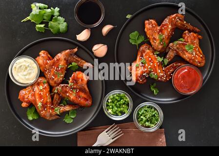 Gebackene Hähnchenflügel auf Teller über dunklem Hintergrund. Draufsicht, flach Stockfoto