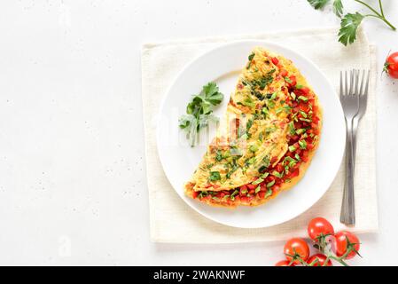 Gefülltes Omelette mit roter Paprika und grüner Zwiebel auf Teller über hellem Steinhintergrund mit Kopierraum. Draufsicht, flach Stockfoto