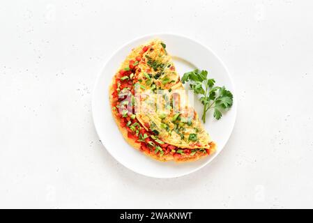 Gefülltes Omelette mit roter Paprika und grüner Zwiebel auf Teller über hellem Steinhintergrund. Draufsicht, flach Stockfoto