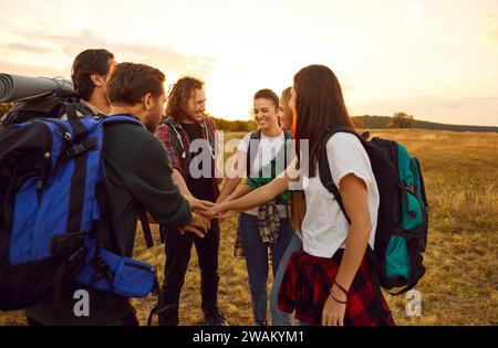 Ein Team glücklicher Wanderer mit Rucksäcken, die im Feld stehen und die Hände zusammenhalten Stockfoto