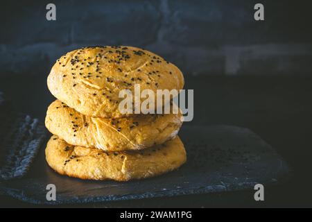 Drei hausgemachte Fladenbrote, Burgerbrötchen, mit schwarzem Kümmel auf dunklem Hintergrund, Kopierraum Stockfoto