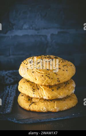 Drei hausgemachte Fladenbrote, Burgerbrötchen, mit schwarzem Kümmel auf dunklem Hintergrund, vertikal mit Kopierraum Stockfoto