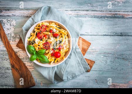 Schüssel mit Pasta, Nudeln, schwäbischer Spätzle, Spinat und Kirschtomaten auf rustikalem Holztisch, Blick von oben Stockfoto