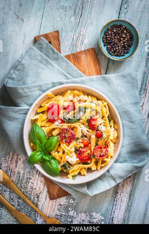 Schüssel mit Pasta, Nudeln, schwäbischer Spätzle, Spinat und Kirschtomaten auf rustikalem Holztisch, Blick von oben Stockfoto