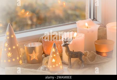 Weihnachtsdekorationen in einem Fenster mit glitzernden Rentieren und verschiedenen Kerzen und Gläsern Stockfoto