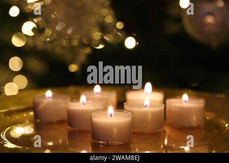Nahaufnahme einer Gruppe brennender Teelichtkerzen auf einem goldenen Teller und vor dunklem Weihnachtshintergrund Stockfoto