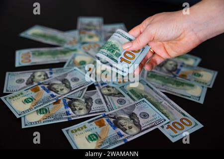 100 Dollar gefaltet in weiblichen Händen. Dollars Bargeld Hintergrundscheine Stockfoto