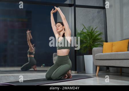 Entspannte, sportliche Frau, die die Arme in einem geräumigen Schlafzimmer streckt. Stockfoto