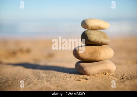 Stillleben. Eine Pyramide aus ausgeglichenen Steinen, die auf Sand vor Meeresgrund gestapelt sind. Gestapelte Kieselsteine. Das Konzept von Balance und Harmonie. Sandstrand, Cal Stockfoto