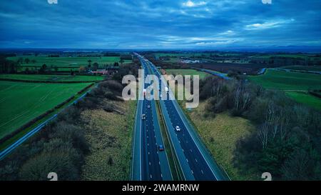 Aus der Vogelperspektive auf eine Autobahn, die durch eine üppige Landschaft unter dem Himmel der Dämmerung führt. Stockfoto