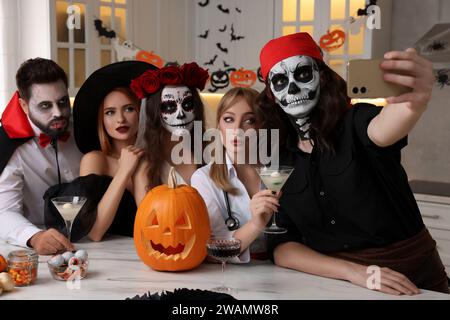 Gruppe von Leuten in gruseligen Kostümen mit Cocktails, die auf der Halloween-Party drinnen Selfie machen Stockfoto