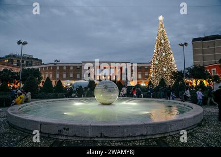 Latina, Italien. Januar 2024. Der Brunnen und im Hintergrund der Weihnachtsbaum mit Weihnachtslichtern für die Weihnachtszeit auf der Piazza del Popolo in Latina. Hunderte jubelnde Kinder und Erwachsene begrüßten die Befana, die anlässlich der Epiphanienfeier in Latina vom Turm des Rathauses abstieg. Quelle: ZUMA Press, Inc./Alamy Live News Stockfoto