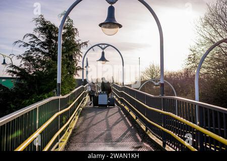 Männliche und weibliche Zugpassagiere Rollen ihre Koffer auf dem Gehweg am örtlichen Bahnhof hoch. Stockfoto