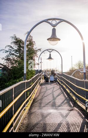 Männliche und weibliche Zugpassagiere Rollen ihre Koffer auf dem Gehweg am örtlichen Bahnhof hoch. Stockfoto