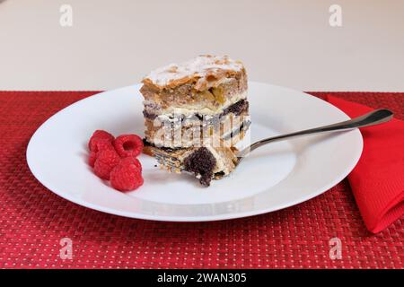 Slowenisches traditionelles Schichtgebäck aus der Provinz Prekmurje. (PREKMURSKA GIBANICA). Der Kuchen sitzt auf einem weißen Teller mit Gabel und Himbeeren. Stockfoto