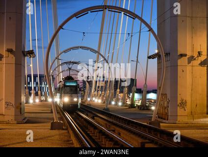 Straßenbahn, die in der Abenddämmerung durch die Kreisbögen der Basarab-Überführungsbrücke in die Statia PASAJ Basarab-Station in Bukarest, Rumänien, ankommt Stockfoto