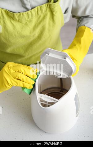 Frau in gelben Handschuhen, die elektrischen Wasserkocher auf einem weißen Tisch reinigt Stockfoto