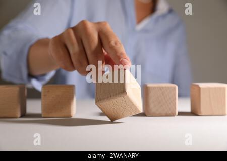 Frau, die Holzwürfel auswählt, unter anderem am weißen Tisch, Nahaufnahme Stockfoto