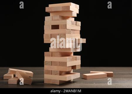 Jenga-Spiel. Turm aus Holzblöcken auf dem Tisch vor schwarzem Hintergrund Stockfoto