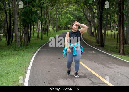 Eine übergewichtige junge Frau, die ihren Schweiß mit der linken Hand beim morgendlichen Trainingslauf auf einer Laufstrecke eines örtlichen Parks abwischt Stockfoto