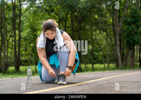 Eine junge, übergewichtige Frau hält an, um ihren Schuh während ihres morgendlichen Trainings auf einer Laufstrecke in einem lokalen Park zu binden Stockfoto