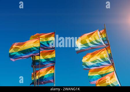 Mehrere farbenfrohe Stolz-Fahnen flattern im Wind vor dem Hintergrund eines hellblauen Himmels energisch Stockfoto