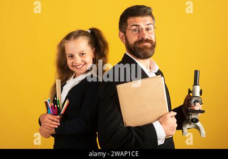 Lehrer mit glücklichen Schüler Schulmädchen. Porträt von lustigen Schulmädchen und Tutor mit Schulbedarf. Glückliche Lehrerin und Schülerin Mädchen auf gelb. Zurück zu Stockfoto