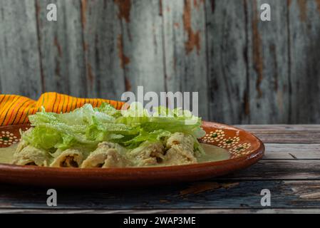 Grüne Enchiladas mit Salat serviert in einer Tonschale auf einem Holztisch. Stockfoto