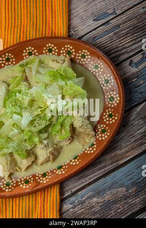 Grüne Enchiladas mit Salat serviert in einer Tonschale auf einem Holztisch. Stockfoto