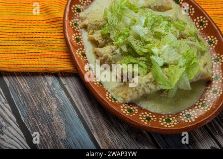 Grüne Enchiladas mit Salat serviert in einer Tonschale auf einem Holztisch. Stockfoto