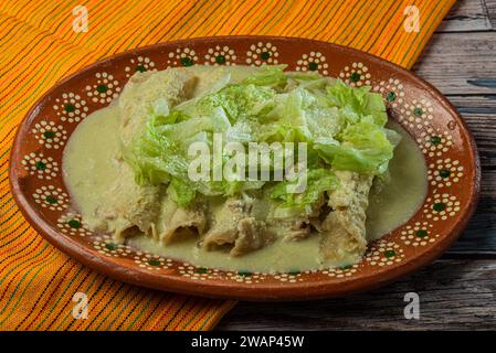 Grüne Enchiladas mit Salat serviert in einer Tonschale auf einem Holztisch. Stockfoto