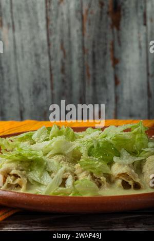 Grüne Enchiladas mit Salat serviert in einer Tonschale auf einem Holztisch. Stockfoto