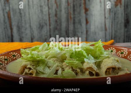 Grüne Enchiladas mit Salat serviert in einer Tonschale auf einem Holztisch. Stockfoto