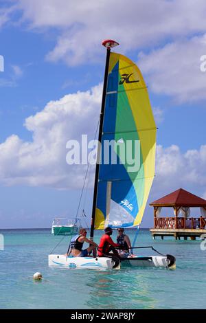 Menschen auf einem farbenfrohen Segelboot im klaren Meer in der Nähe eines Stegs mit einem Pavillon unter blauem Himmel, Dominicus Beach, Bayahibe, Dominikanische Republik, HISP Stockfoto