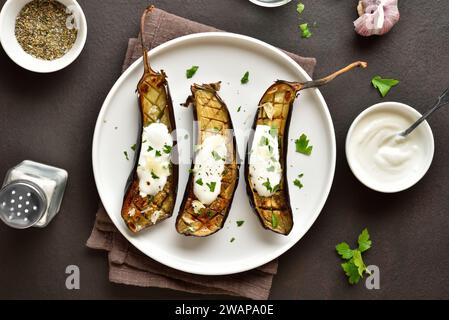 Geröstete Aubergine mit Knoblauch-Joghurt-Dressing auf Teller auf dunklem Hintergrund. Draufsicht, flach Stockfoto