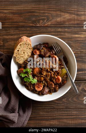 Gedünsteter Kohl (polnische Bigos) mit Sauerkraut, Pilzen, geräuchertem Fleisch und Gewürzen in einer Schüssel auf hölzernem Hintergrund. Draufsicht, flach Stockfoto