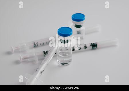 Zwei Durchstechflaschen mit Impfstoff mit blauen Kappen und Spritzen Stockfoto