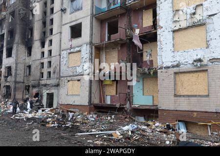 Die Fassade eines Gebäudes, das durch eine russische Raketenexplosion beschädigt wurde. Schutthaufen und kaputte Fenster, die vorübergehend mit Holzpaneelen bedeckt sind, sind in der Nähe des Gebäudes zu sehen Stockfoto