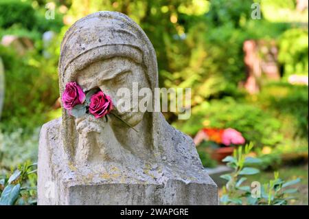 Die Trauerstatue mit betenden Händen und Blumen vor Gräbern Stockfoto
