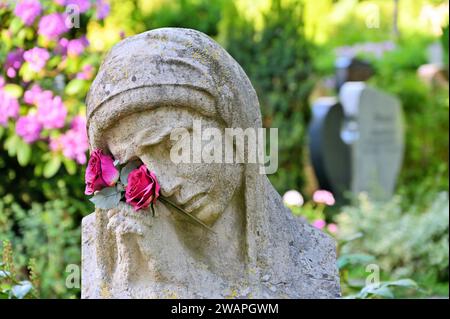 Die Trauerstatue mit betenden Händen und Blumen vor Gräbern Stockfoto