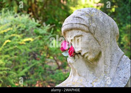 Die Trauerstatue mit betenden Händen und Blumen vor Gräbern Stockfoto