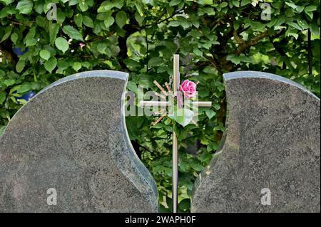 Grabstein mit Metallkreuz und Rose in der Mitte Stockfoto