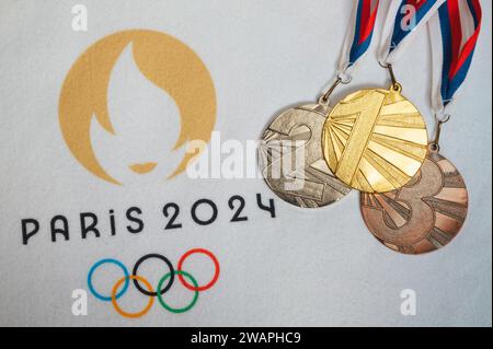 PARIS, FRANKREICH, DEZEMBER. 4. 2023: Logo des olympischen Sommerspiels in Paris 2024 und Gewinnermedaillensatz. Goldene Silber- und Bronzemedaille. Weißer Hintergrund. Stockfoto