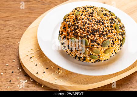 Hoher Blickwinkel auf Burgerbrötchen, bestreut mit weißem und schwarzem Sesam und Kürbissamen in weißer Keramikplatte auf Holzbrett auf hölzernem Hintergrund. Stockfoto