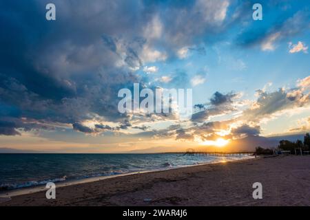 Farbenfroher Sonnenuntergang auf dem Meer. Bergsee in den Strahlen der orangen Sonne. Kirgisistan, Issyk-Kul-See. Natürlicher Hintergrund. Querformat Stockfoto